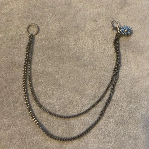 Dubbel kedja med blomdetalj - Snygg dubbel kedja i silverfärg med en unik blomdetalj i blått. Perfekt som accessoar för att ge din outfit en extra edge. Kedjan har en ring och en karbinhake för enkel fastsättning.
