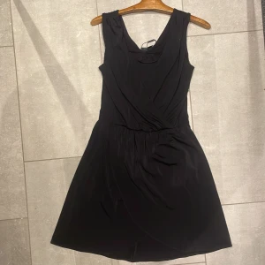 Svart kortklänning från Vero Moda - Snygg svart kortklänning från Vero Moda i storlek XS. Klänningen är ärmlös med en omlott-design framtill som ger en elegant touch. Perfekt för olika tillfällen och lätt att matcha med accessoarer.