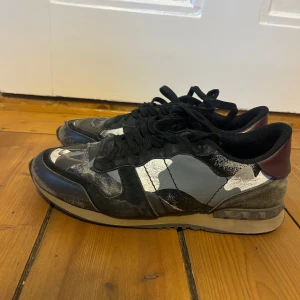 Valentino rockrunners  - Snygga sneakers från Valentino med ett coolt camouflage-mönster i svart, grått och vitt. Skorna har snörning och en unik design med röda  detaljer på hälen!. Perfekta för dig som vill sticka ut! Priset är ej hugget i sten! Storlek 41,5 passar 42-43