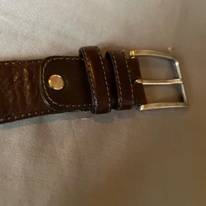 Brunt läderbälte från Portia - Snyggt brunt läderbälte från Portia, handgjort i Italien. Bältet har en klassisk design med en silverfärgad spänne och flera justeringshål för perfekt passform. Perfekt för att ge en stilren touch till din outfit nytt så kostade det 509 och nu säljer jag de för 1 75 kr.