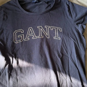 Svart t-shirt från GANT - Säljer en stilren svart t-shirt från GANT med deras logga tryckt i vitt på bröstet. Perfekt för en avslappnad look.