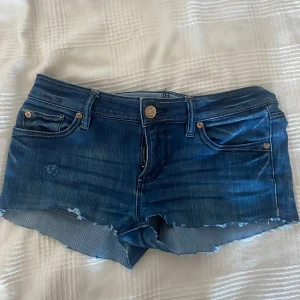 Lågmidjade jeansshorts - Snygga mörkblå, lågmidjade  jeansshorts med fransiga kanter. De är i storlek 34 med midjemåttet rakt över 38cm. De har även lite egengjorda slitningar på vardera ben.💞