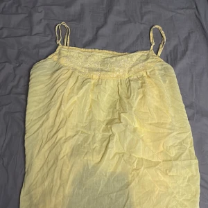 Gul ärmlös linnetopp - Säljer en söt gul linnetopp med smala axelband och spetsdetaljer upptill. Perfekt för varma sommardagar. Toppen är luftig och bekväm att bära.