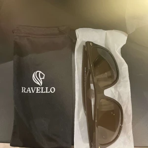 Bruna solglasögon från Ravello - Snygga bruna solglasögon från Ravello med en klassisk design. De har en solid brun färg och kommer med ett praktiskt fodral för förvaring. Perfekta för soliga dagar! Pris kan diskuteras, helt oanvända men kommer inte till användning.