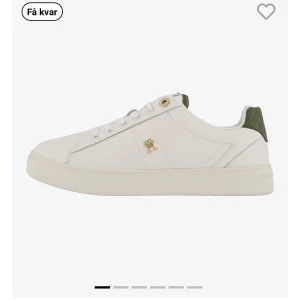 Vita sneakers med gröna detaljer - Snygga vita sneakers med gröna detaljer och guldfärgad logotyp på sidan. Skorna har en klassisk design med snörning och en bekväm sula. Perfekta för en stilren look.