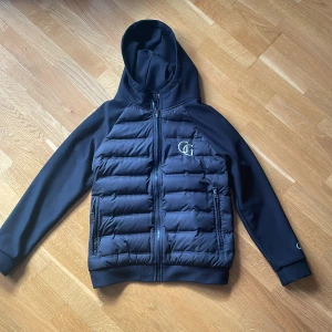 Svart cardigan från Garde Grisch - Snygg svart cardigan från Garde Grisch med huva och dragkedja. Jackan har en quiltad design på framsidan och baksidan, samt långa ärmar. Perfekt för kyligare dagar. Nypris 1800kr