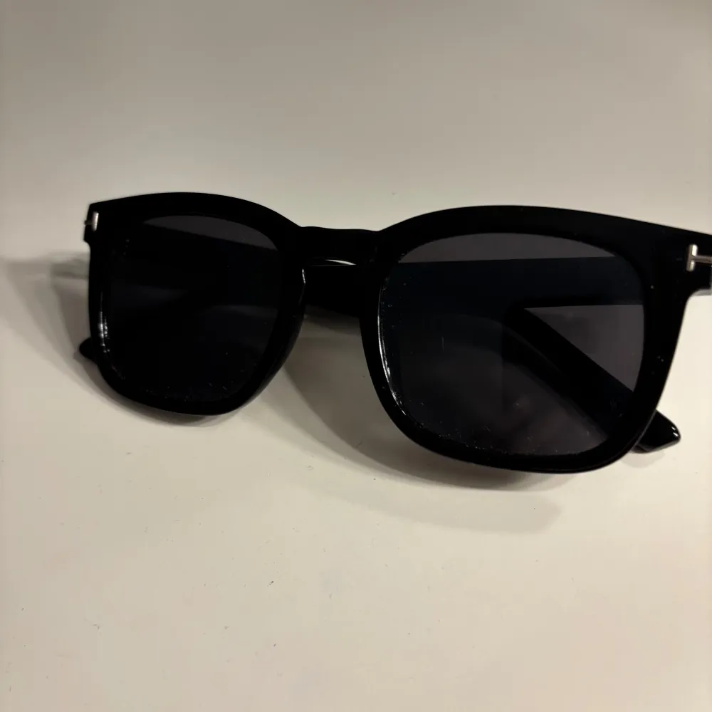 Snygga svarta solglasögon med en klassisk fyrkantig form. Perfekta för att ge en stilren look. De har en solid svart färg och breda skalmar för extra komfort.. Asusteet.