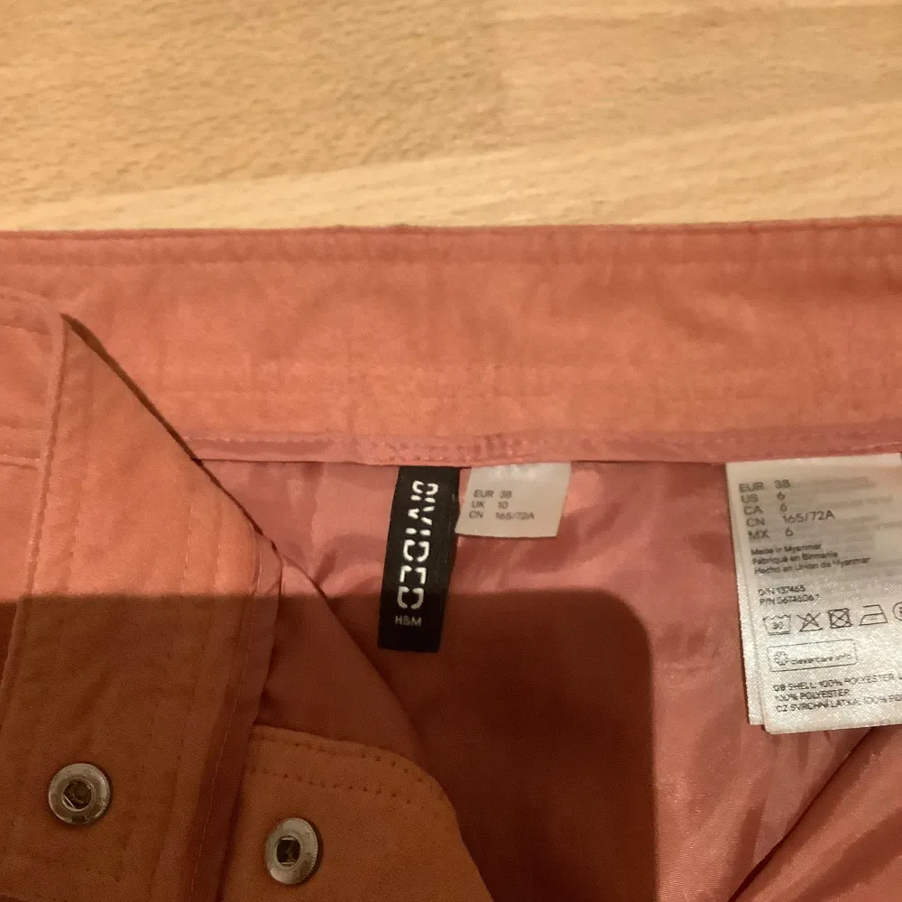 Snygg mockakjol kortkjol från H&M Divided med knappar framtill. Perfekt för en trendig look. Kjolen har en A-linjeformad passform och är tillverkad i ett mjukt material.. Hameet.