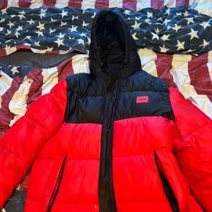 Röd och svart pufferjacka från Hugo - Säljer en snygg röd och svart pufferjacka från Hugo. Jackan har en huva och dragkedja framtill. Perfekt för kyliga dagar med sin stilrena design och varma material.