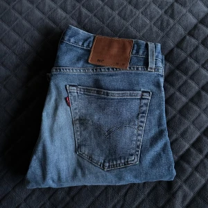 Blå jeans från Levi's - Säljer ett par klassiska blå jeans från Levi's. De har en rak passform och är tillverkade i slitstarkt denim. Perfekta för en avslappnad stil. Jeansens ikoniska lädermärke syns tydligt på baksidan.