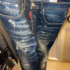 Blå jeans från Dsquared2 - Snygga blå jeans från Dsquared2 med slitna detaljer och färgstänk i olika nyanser. De har en klassisk femficksdesign och en gul etikett på baksidan. Perfekta för en trendig och avslappnad stil. De är endast använda 2 ggr, kom med bud! 