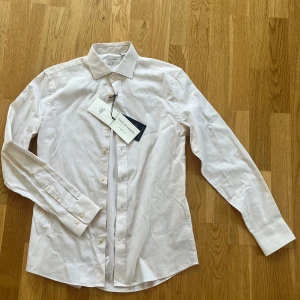 Oanvänd Tiger of Sweden skjorta - Säljer en stilren vit skjorta från Tiger of Sweden i slim fit. Perfekt för bal och student. Aldrig använd och skickas med lappen på. Nypris är 1399kr. 