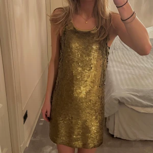 Guldglittrig klänning - Säljer en glittrig guldklänning. Den är ärmlös och har en rak passform som ger en elegant look. Perfekt för festliga tillfällen. Klänningen har en rund halsringning och är täckt med paljetter som ger en lyxig känsla 🧡sliten i dragkedjan men inget som gör den ofungerande