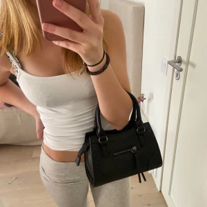 Svart handväska med dragkedja - Snygg svart handväska med praktisk dragkedja framtill. Väskan har både handtag och en avtagbar axelrem för flexibilitet. Aldrig använd! Pris kan diskuteras❣️