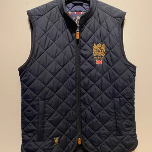 Mörkblå quiltad väst från Morris - Snygg mörkblå quiltad väst från Morris. Västen har dragkedja framtill och är perfekt för en stilren look. Passar bra till både casual och mer uppklädda tillfällen.