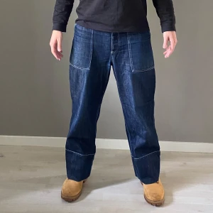 Kenzo jeans med hög midja i kontrastsöm - Snygga blå jeansbyxor med stora fram- och bakfickor. Byxorna har en loose passform och är perfekta för en avslappnad stil. De har en klassisk highwaist och är tillverkade i slitstarkt denimtyg. Skick 7/10