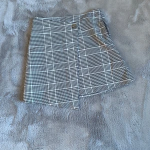 Rutig kjol från H&M - Snygg rutig kjol från H&M i svart och vit med dragkedja och knappdetalj. Perfekt för en stilren look.