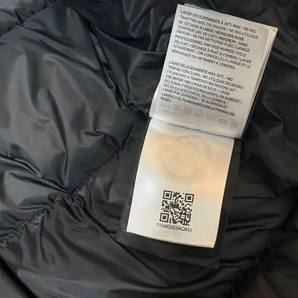 Snygg svart pufferjacka från Moncler med huva och dragkedja. Jackan har ett quiltat mönster och en broderad logotyp på ärmen. Perfekt för kyliga dagar med sin stilrena design och varma material.. Takit.