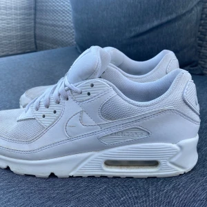 Vita Nike Air Max sneakers - Säljer ett par vita Nike Air Max sneakers med klassisk design och synlig luftdämpning i sulan. Skorna har snörning och en rund tå, vilket ger en bekväm passform. Perfekta för både vardag och träning.