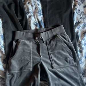 Grå byxor från Juicy Couture - Snygga grå mjukisbyxor från Juicy Couture med snörning i midjan och praktiska fickor både fram och bak. Byxorna har en broderad logga på framsidan och är perfekta för en avslappnad stil.