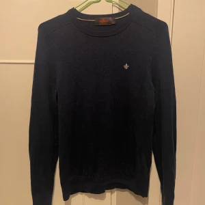 Mörkblå tröja i merinoull från Morris - Säljer en stilren mörkblå tröja från Morris i 100% merinoull. Tröjan har en liten broderad detalj på bröstet och långa ärmar. Perfekt för kyligare dagar.