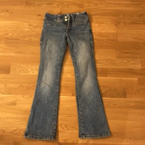 Blå bootcut jeans - Snygga blå bootcut jeans med två knappar och dragkedja fram. De har fickor med lock och knappdetaljer bak. Perfekta för en avslappnad stil. Kom med förlag om pris ifall de inte passar.