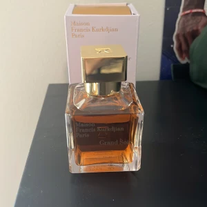 Grand Soir Eau de Parfum från Maison Francis Kurkdjian - Exklusiv parfym Grand Soir från Maison Francis Kurkdjian i en elegant glasflaska med gyllene lock. Doften är varm och sofistikerad, perfekt för speciella tillfällen. Flaskan rymmer 70 ml och kommer i en stilren vit förpackning med guldtext. Endast använd vid 2 tillfällen.