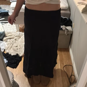Svart långkjol - Säljer en stilren svart långkjol med elastisk midja. Perfekt för en avslappnad look eller att klä upp med en snygg topp. Kjolen har en mjuk och bekväm passform