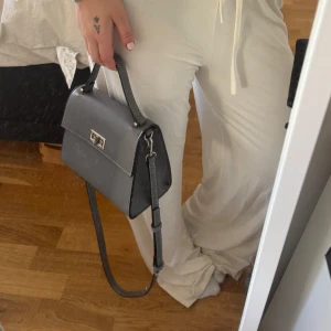 Grå axelväska med silverdetaljer GinaTricot - ALDRIG ANVÄND! Snygg grå axelväska från GinaTricot med justerbar axelrem och stiliga silverdetaljer. Väskan har ett praktiskt lås framtill och är perfekt för att bära dina nödvändigheter. Enkel och elegant design som passar till många olika outfits.
