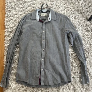 Grå skjorta från Jack & Jones - Snygg grå skjorta från Jack & Jones med klassisk krage och vita knappar. Perfekt för en stilren look. Skjortan har långa ärmar och en diskret randig insida av kragen.