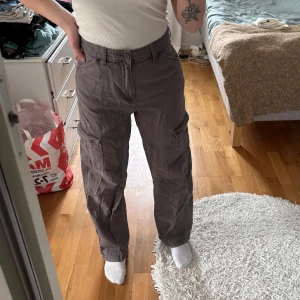 Grå/bruna cargobyxor - Säljer ett par grå/bruna cargobyxor med flera praktiska fickor. Byxorna har en loose passform och är perfekta för en avslappnad stil. De är tillverkade i ett slitstarkt material och har en midwaist design.