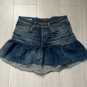 Snygg Jeanskjol  - Snygg jeanskjol med volangdetalj. Kjolen har en klassisk blå denimfärg och femficksdesign. Perfekt för en avslappnad stil.