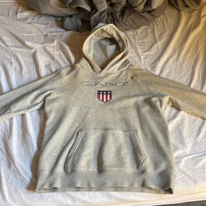 Grå hoodie från GANT - Säljer en stilren grå hoodie från GANT med deras ikoniska logga och emblem på bröstet. Tröjan är lite missfärgad har haft den i några år nu men de är inget som man tänker på. Passar dom som har M/s i skorlek skulle säga Xs också. Pris kan diskuteras 😁