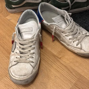 Vita sneakers från Philippe Model - Snygga vita sneakers från Philippe Model med blå och röda detaljer. Skorna har snörning och en rund tå, vilket ger en klassisk look. Perfekta för en avslappnad stil.