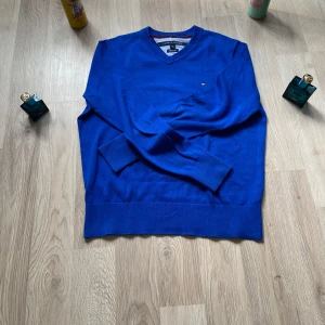 Blå tröja från Tommy Hilfiger - Säljer en snygg blå tröja från Tommy Hilfiger i mjuk Pima bomull. Tröjan har en v-ringning och ett litet broderat logotypmärke på bröstet. Perfekt för en stilren look. Nästan helt oanvändi storlek S.