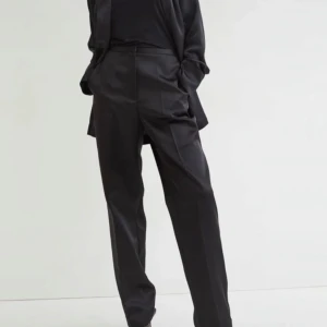 Svarta kostymbyxor från H&M - Snygga svarta kostymbyxor från H&M i återvunnen polyester och viskos. Byxorna har en klassisk rak passform och hög midja, perfekt för en stilren look. De har diskreta fickor och en elegant design som passar till många tillfällen.storlek 42.nyskick med lappar 