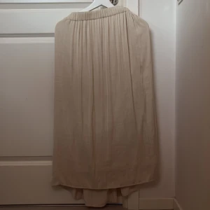 Beige långkjol från Gina Tricot - Säljer en stilren beige långkjol från Gina Tricot. Kjolen har en elastisk midja och ett flödande fall som ger en elegant look. Perfekt för både vardag och speciella tillfällen.