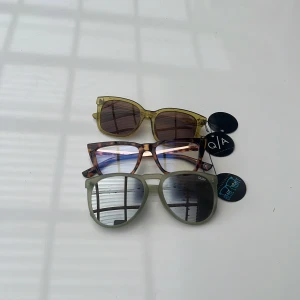 Tre trendiga glasögon från Quay Australia - Säljer tre par glasögon från Quay: ett par solglasögon med transparent gul fyrkantig båge och bruna linser, ett par blåljusglasögon med brunmelerad rektangulär båge i leopardmönster, samt ett par solglasögon med ljusgrön rundad båge och spegelglas.