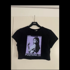 Svart croppad Ariana Grande topp H&M - Svart croppad topp från H&M Divided med Ariana Grande-tryck och lila motiv från Positions. T-shirten har korta ärmar och rund hals. 