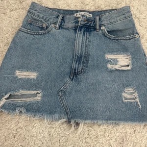 Blå jeanskjol från Pull&Bear - Snygg ljusblå jeanskjol från Pull&Bear med slitna detaljer och fransig nederkant. Klassisk femficksmodell med bälteshällor och dragkedja fram. Perfekt för dig som gillar en avslappnad och trendig stil.