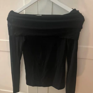 Svart offshoulder topp - Snygg svart offshoulder topp med långa ärmar och bred krage som vilar över axlarna. Perfekt för dig som vill ha en stilren och trendig look. Toppens passform är figurnära och materialet känns mjukt mot huden.