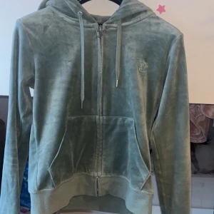 Ljus grön velour tröja Juicy Couture - Supermjuk mintgrön hoodie från Juicy Couture i velour. Klassisk modell med dragkedja, huva och känguruficka framtill. Snygga snören i huvan och diskret Juicy couture logga på bröstet. Perfekt för en chill och trendig look. Nästan oanvänd, finns juicy byxor i samma färg i XXS skriv  om de önskas så lägger jag ut dem på min PLICK med!💓