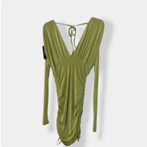 Grön från NA-KD - Snygg grön kortklänning från NA-KD med djup v-ringning, långa ärmar och trendig snörning i ryggen. Klänningen har draperade detaljer och är tillverkad i ett glansigt, stretchigt material som ger en lyxig känsla. Perfekt för dig som vill sticka ut.
