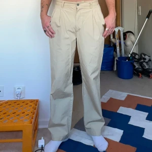 Beiga chinos från Boomerang - Snygga beiga chinos från Boomerang i 100% bomull. Klassisk rak passform med pressveck, hällor för bälte och knäppning fram. Fickor både fram och bak, diskret logga ovanför bakfickan. Perfekta för en clean och stilren look. Finns en orange fläck på vänstra baksidan, inget som märks vid användning. Ska försöka få bort i tvätt. De sitter som en W32 L32