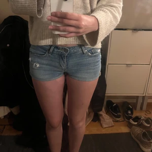 Levi's ljusblå jeansshorts low waist - Säljer ett par snygga ljusblå jeansshorts från Levi's med låg midja och klassisk femficksdesign. Shortsen har slitna detaljer framtill. Perfekta till sommaren och passar till allt. Levi's logga bak på linningen och röd etikett på bakfickan.
