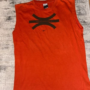 Vintage Nike ärmlös röd Dri-Fit t-shirt - Vintage Nike Dri-Fit t-shirt i starkt röd färg med ärmlös design. Tryck i svart framtill med japanska tecken och Nike-logga. Perfekt för träning eller basket, tillverkad i funktionsmaterial som andas.