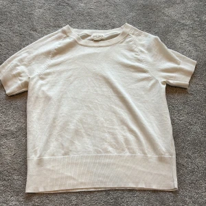 Vit kortärmad tröja Holly & Whyte - En stilren vit kortärmad tröja från Holly & Whyte by Lindex. Tröjan har rund halsringning och breda ribbade muddar vid ärmslut och nederkant. Perfekt för en clean och enkel look, lätt att matcha med allt.