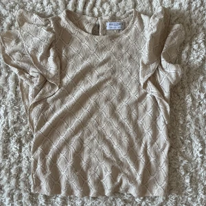 Beige blus med volangärm  - Supersöt beige blus från Holly & Whyte med korta volangärmar och diskret rutmönster i strukturen. Som ny 💗