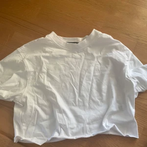 Vit croppad t-shirt från Bik Bok - En basic vit croppad t-shirt från Bik Bok i mjuk bomull. T-shirten har korta ärmar, rund halsringning och en avslappnad passform. Perfekt att matcha med jeans eller kjol för en clean och enkel look.