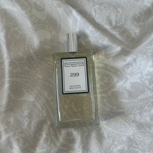 The Essence Vault 299 Eau de Parfum - Snygg parfymflaska från The Essence Vault, modell 299. Flaskan är rektangulär i genomskinligt glas med silverfärgad spraykork och svartvit etikett. Innehåller 100 ml Eau de Parfum. Perfekt för dig som gillar stilrena och minimalistiska doftflaskor. Extremt god och vädligt unik.